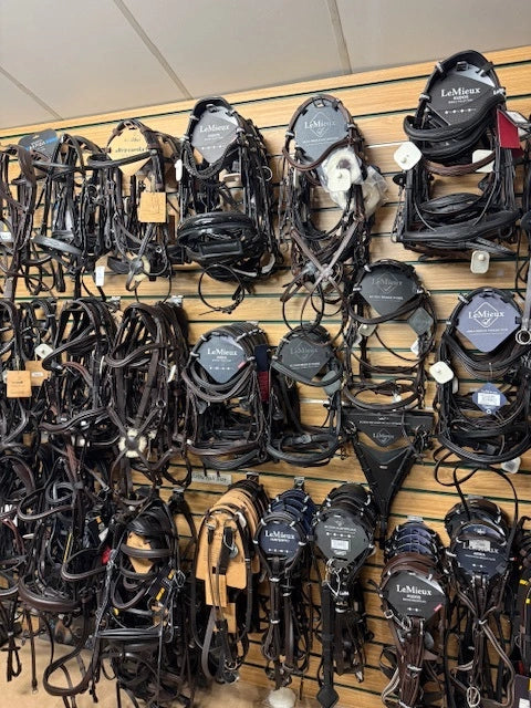 Collection of horse bridles and halters on a wooden rack.